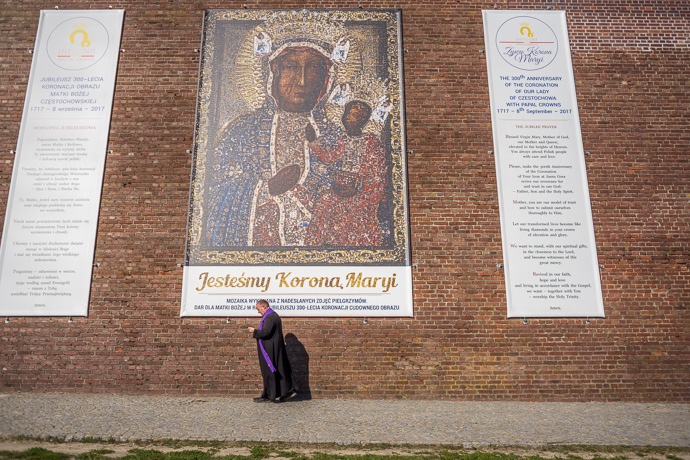 Celebration of Maria ascension in Jasna Góra, Poland 2018. A priest walks along a fortress wall on which banners have been hung. Image: Michel Meijer