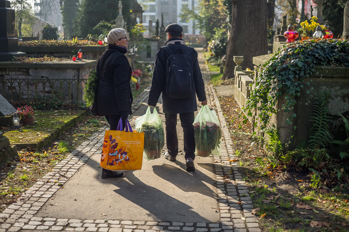 All Saints' Day at Rakowicki Cemetery in Kraków, Poland 2019. A couple carries plastic bags full of flowers across the cemetery, All Saints' Day in Poland. Image: Michel Meijer