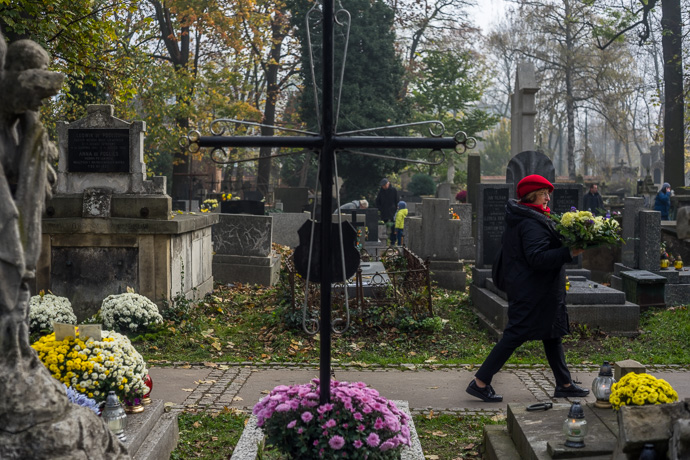 All Saints' Day at Rakowicki Cemetery in Kraków, Poland 2019. A woman with a red hat and a bouquet of flowers in her hands is walking through the cemetery, All Saints' Day in Poland. Image: Michel Meijer