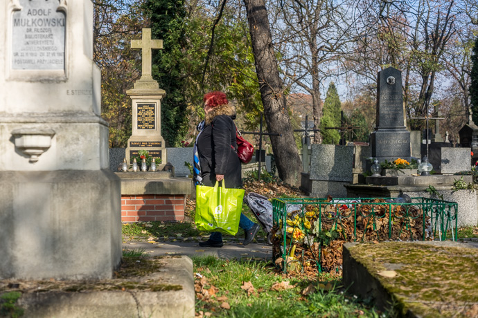 All Saints' Day at Rakowicki Cemetery in Kraków, Poland 2019. A woman walks through the cemetery carrying a bag and trolley filled with candles and flowers, All Saints' Day in Poland. Image: Michel Meijer
