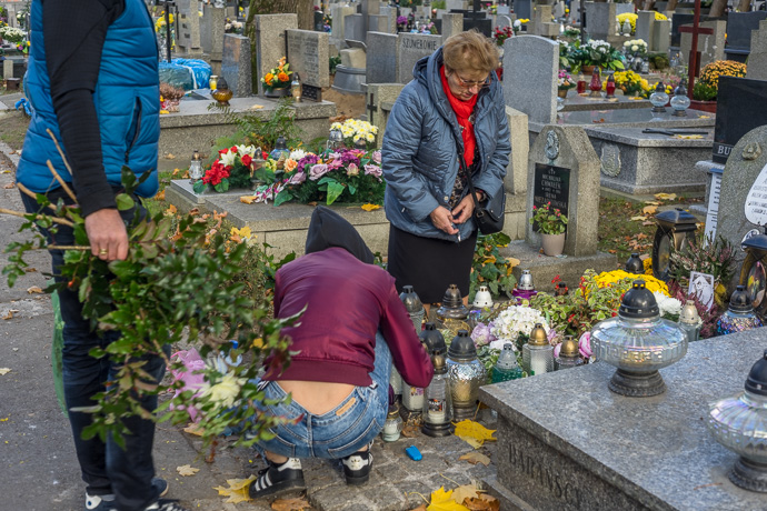 All Saints' Day at Rakowicki Cemetery in Kraków, Poland 2019. A family lays flowers and places candles on a grave, All Saints' Day in Poland. Image: Michel Meijer