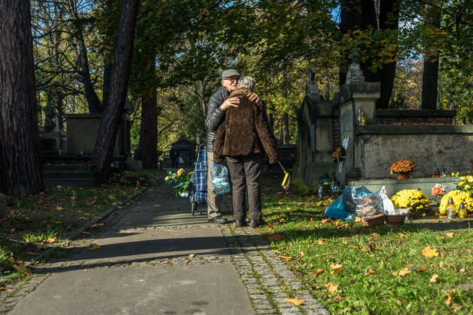 All Saints' Day at Rakowicki Cemetery in Kraków, Poland 2019. A man embraces a woman who is cleaning a grave, All Saints' Day in Poland. Image: Michel Meijer
