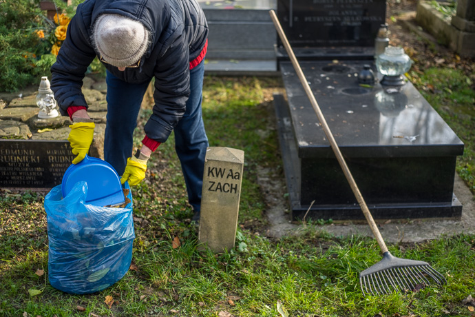 All Saints' Day at Rakowicki Cemetery in Kraków, Poland 2019. A woman clears away leaves that have fallen around and on a grave, All Saints' Day in Poland. Image: Michel Meijer