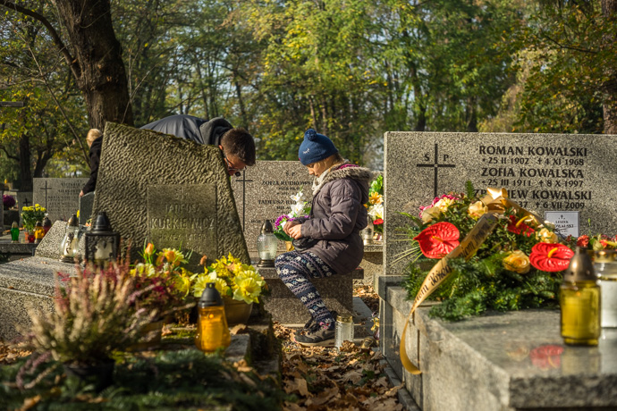 All Saints' Day at Rakowicki Cemetery in Kraków, Poland 2019. Father and daughter clean a grave and place candles on it, All Saints' Day in Poland. Image: Michel Meijer