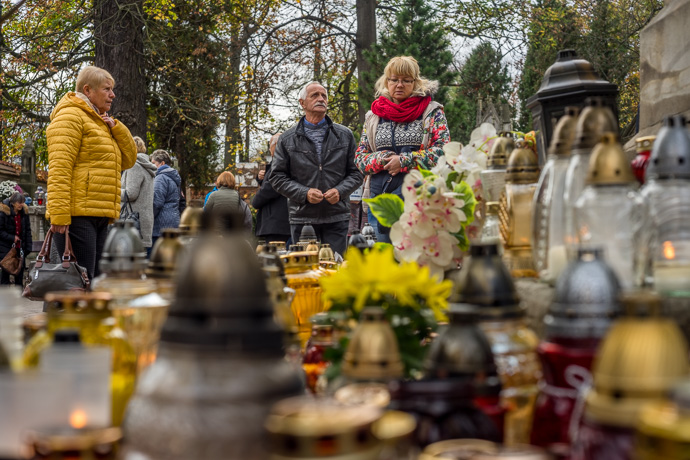 All Saints' Day at Rakowicki Cemetery in Kraków, Poland 2019. People stop at a monument under which hundreds of candles are placed, All Saints' Day in Poland. Image Michel Meijer