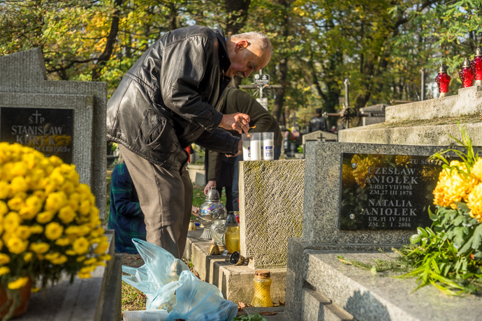 All Saints' Day at Rakowicki Cemetery in Kraków, Poland 2019. A man lights a number of candles on a tombstone, All Saints' Day in Poland. Image: Michel Meijer