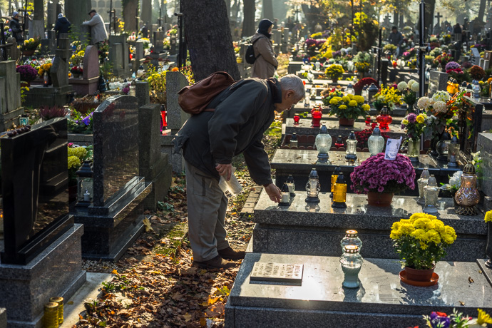 All Saints' Day at Rakowicki Cemetery in Kraków, Poland 2019. A man puts a candle on a tombstone, All Saints' Day in Poland. Image: Michel Meijer