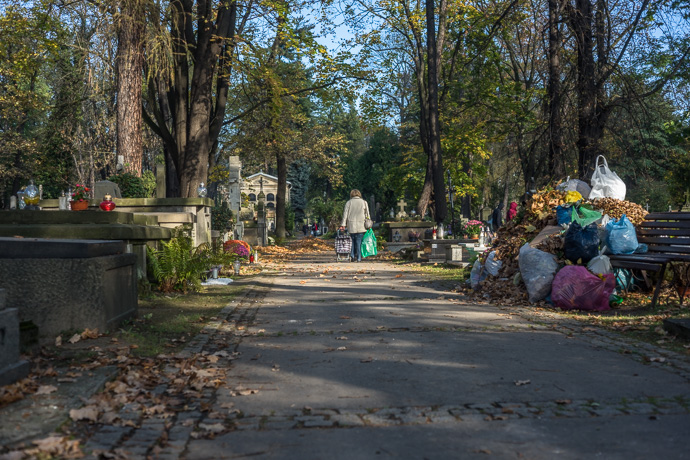 All Saints' Day at Rakowicki Cemetery in Kraków, Poland 2019. A woman walks through the cemetery with a trolley and a green plastic bag in her hand, All Saints' Day in Poland. Image: Michel Meijer