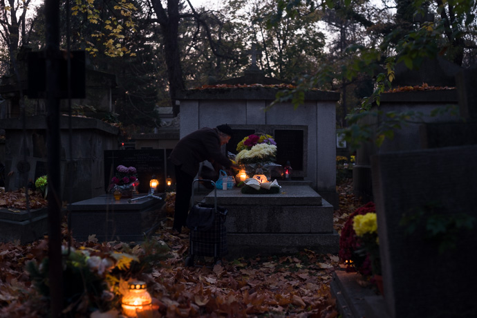 All Saints' Day at Rakowicki Cemetery in Kraków, Poland 2019. An old woman places flowers and candles on a tombstone, All Saints' Day in Poland. Image: Michel Meijer