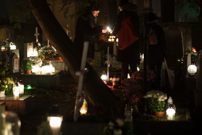 All Saints' Day at Rakowicki Cemetery in Kraków, Poland 2019. People light candles above a grave stone in a cemetery, All Saints' Day in Poland. Image: Michel Meijer