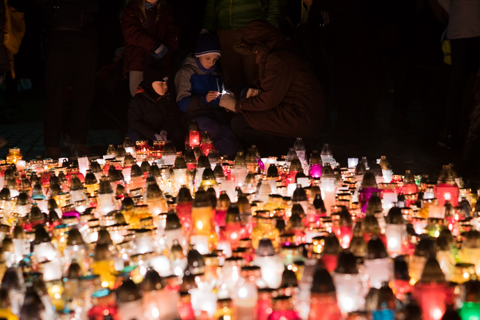 All Saints' Day at Rakowicki Cemetery in Kraków, Poland 2019. A child lights a candle under the direction of his mother, All Saints' Day in Poland. Image: Michel Meijer