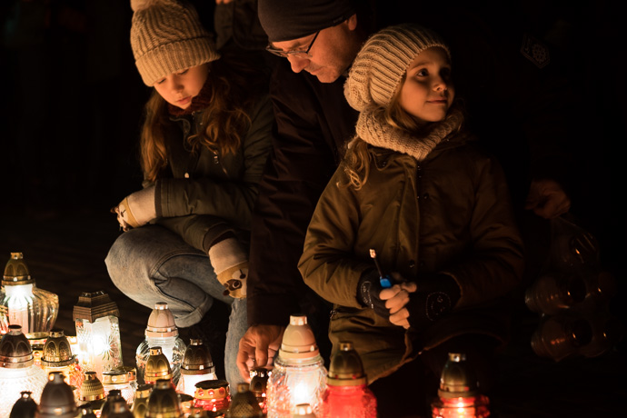 All Saints' Day at Rakowicki Cemetery in Kraków, Poland 2019. A father and his two daughters light a candle, All Saints' Day in Poland.  Image: Michel Meijer