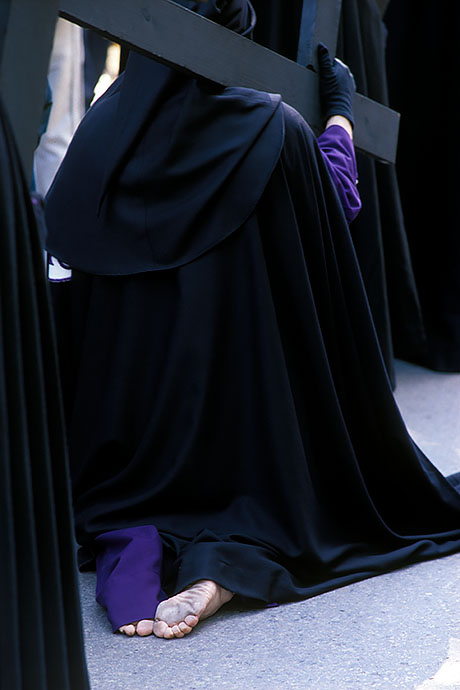 A barefoot penitent carries a wooden cross on his shoulder and kneels on the ground in the procession. Image: Michel Meijer