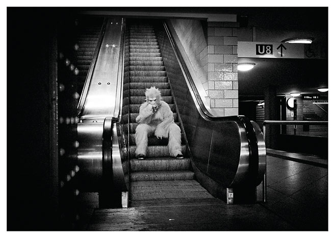 Eine Person in einem Gorillakostüm sitzt auf einer Rolltreppe in einem Berliner U-Bahnhof. Das Foto wurde von Christian Reister aufgenommen.