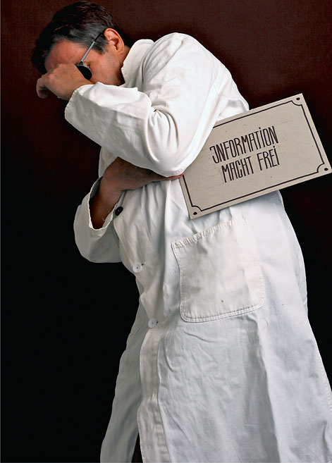 Ein Mann in einem Laborkittel und mit einem Schild in der Hand verbirgt sein Gesicht. Eine Arbeit von Marcel Schock.